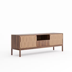 Può includere: Una moderna consolle multimediale a basso profilo con finitura in noce caldo. L'armadio presenta due ante con un design geometrico a intarsio in legno chiaro, un ripiano centrale aperto e un cassetto con pomello color ottone. La consolle è sostenuta da quattro gambe sottili e tinte scure.