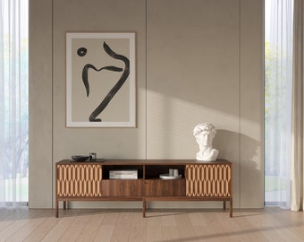May include: A mid-century modern style wooden media console with two doors and open shelving. The console has a light wood finish with a geometric pattern on the doors. The console is sitting on a light wood floor in front of a beige wall with a framed abstract art print.
