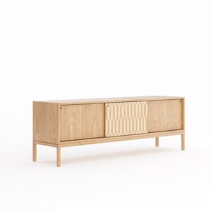 Può includere: Un mobile in legno chiaro con due ante scorrevoli. Il mobile ha un motivo geometrico su una delle ante e maniglie in ottone. Il mobile è appoggiato su quattro gambe.