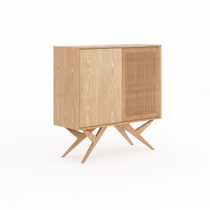 May include: A light wood cabinet with two doors, one solid and one with vertical slats. The cabinet is on four angled legs.