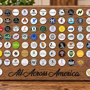 May include: A rectangular wooden display board featuring a grid of numerous circular golf ball markers, each with unique logos and text. The bottom of the board is engraved with the cursive text All Across America, showcasing a collection of golf course memorabilia.