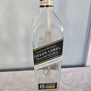 May include: A clear glass bottle with a black label that reads "Johnnie Walker - Green Label Blended Malt Scotch Whisky". The label also includes the text "Aged 15 Years".