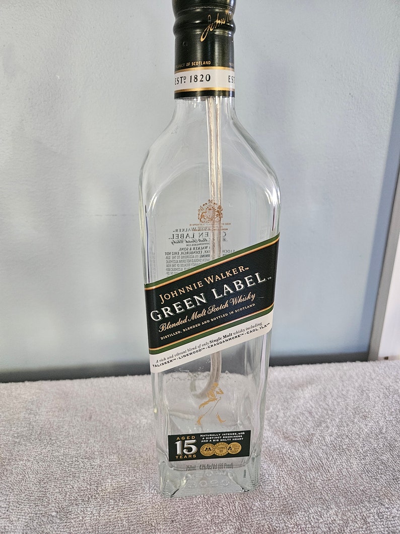 May include: A clear glass bottle with a black label that reads "Johnnie Walker - Green Label Blended Malt Scotch Whisky". The label also includes the text "Aged 15 Years".