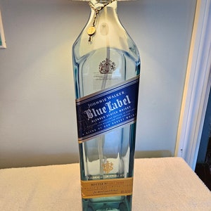 May include: A clear glass bottle with a blue label that reads "JOHNNIE WALKER Blue Label BLENDED SCOTCH WHISKY" and "A BLEND OF OUR RAREST WHISKIES". The bottle has a gold cap and a gold label on the bottom that reads "BOTTLE NO. 14388".