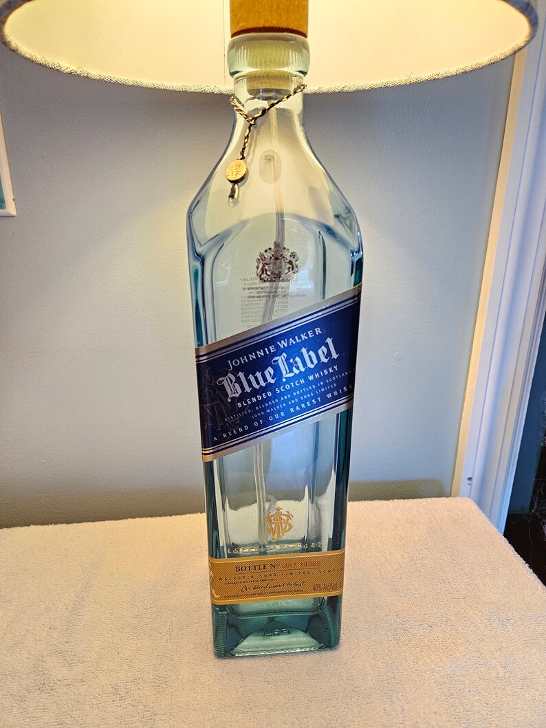 May include: A clear glass bottle with a blue label that reads "JOHNNIE WALKER Blue Label BLENDED SCOTCH WHISKY" and "A BLEND OF OUR RAREST WHISKIES". The bottle has a gold cap and a gold label on the bottom that reads "BOTTLE NO. 14388".