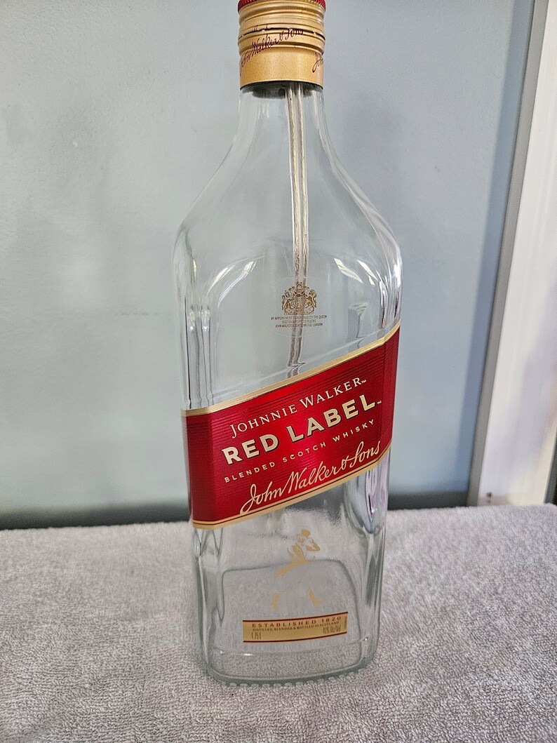 May include: Empty glass bottle with a red label that says "JOHNNIE WALKER - RED LABEL BLENDED SCOTCH WHISKY John Walker & Sons ESTABLISHED 1820"