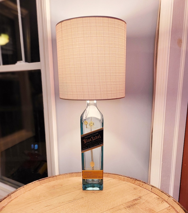 May include: A lamp made from a clear glass bottle with a gold label that reads "Johnnie Walker Blue Label" and a white fabric lampshade.