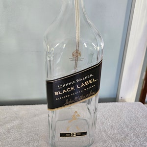 May include: Empty glass bottle with a black label that reads "Johnnie Walker Black Label Blended Scotch Whisky John Walker & Sons Aged 12 Years".