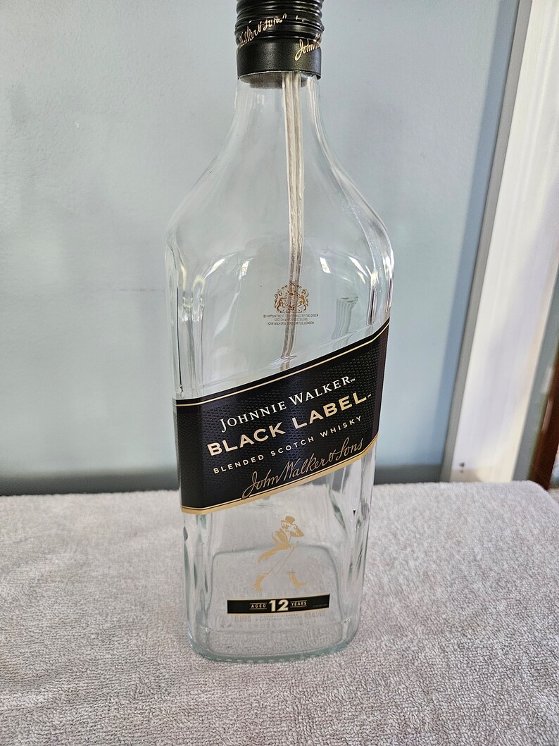 May include: Empty glass bottle with a black label that reads "Johnnie Walker Black Label Blended Scotch Whisky John Walker & Sons Aged 12 Years".