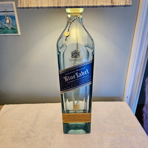 May include: A clear glass bottle lamp with a blue and gold label that reads "Johnnie Walker Blue Label Blended Scotch Whisky". The bottle is sitting on a white surface.