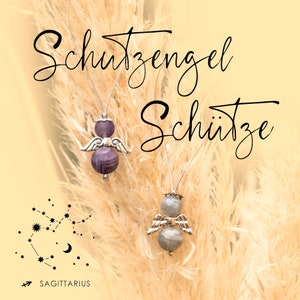 Könnte beinhalten: Zwei silberne Engelsanhänger mit Flügeln, einer mit einem violetten Amethyststein und der andere mit einem grauen Stein. Die Anhänger hängen an einer Schnur und befinden sich vor einem beigefarbenen Hintergrund mit dem Text "Schutzengel Schütze" und einem Schützen-Sternbild.