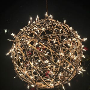 May include: A large, round, twig sphere with white string lights wrapped around it. The sphere is hanging from the ceiling and is lit up against a dark background.