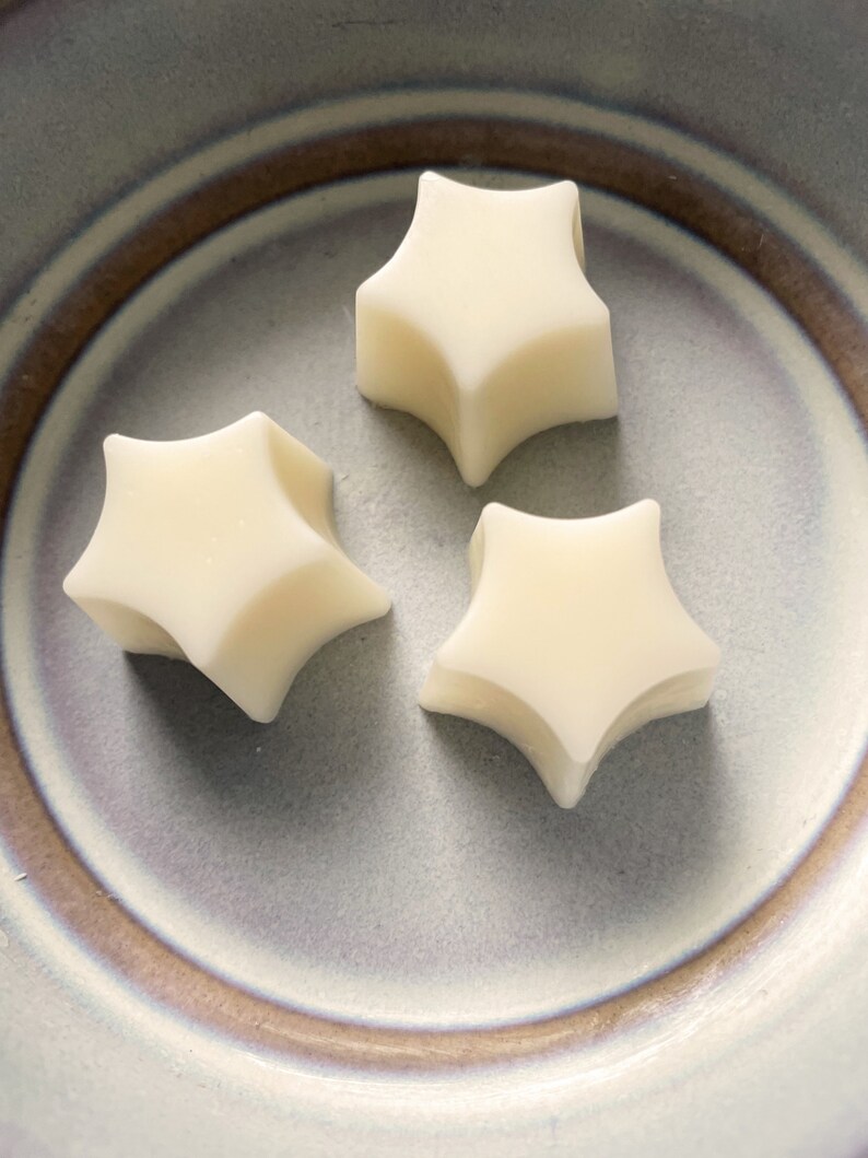 Pu&ograve; includere: Tre cere di cera a forma di stella bianca su un piatto in ceramica grigio e marrone.