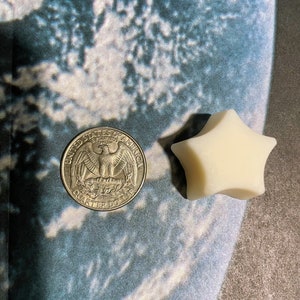 May include: A silver US quarter dollar coin with an eagle design and the words "United States of America" and "Quarter Dollar" on it, next to a white star-shaped candle.