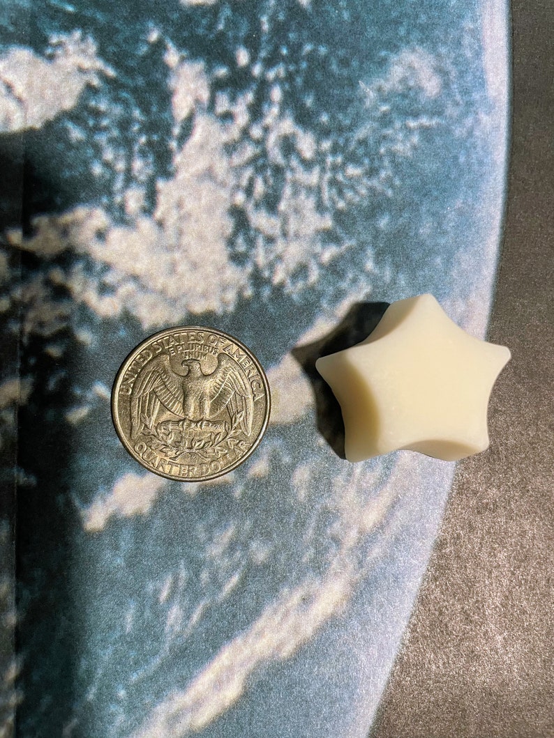 May include: A silver US quarter dollar coin with an eagle design and the words "United States of America" and "Quarter Dollar" on it, next to a white star-shaped candle.