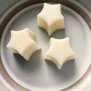 May include: Three white star-shaped wax melts on a gray and brown ceramic plate.