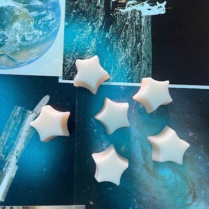 May include: Six white star-shaped wax melts on a blue and black background with a space theme.