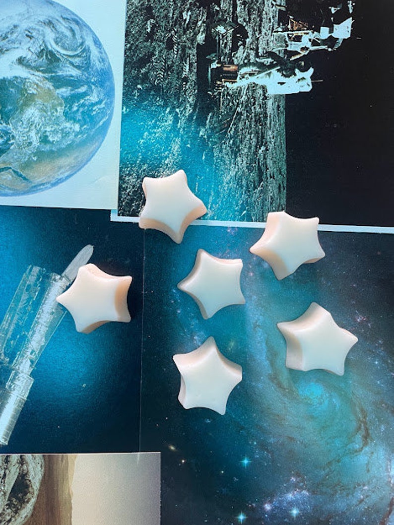 May include: Six white star-shaped wax melts on a blue and black background with a space theme.