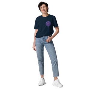 Op de afbeelding: Een marineblauw t-shirt met een ronde paarse afbeelding op de linkerborst. De afbeelding heeft een gestileerd ontwerp met de tekst "FOREVER" in de cirkel.