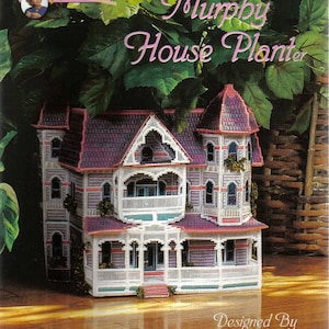 May include: A plastic canvas house planter kit, featuring a detailed Victorian-style house with a purple roof, white trim, and a wraparound porch. The kit is labelled "Murphy House Planter" and designed by Sandi Tucker.