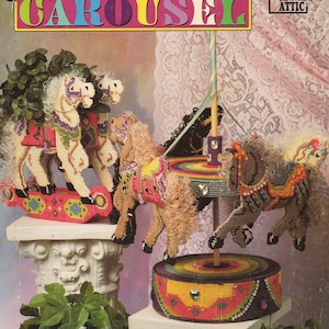 May include: A plastic canvas pattern for a carousel, with three horses and a central pole. The horses have decorative details and sit on a circular base. The text "Magical Motion Carousel" is displayed at the top of the image.