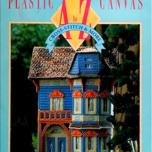May include: A plastic canvas house craft project. The house is blue, orange, and tan, with a detailed roof and window awnings. The text on the cover reads "Vanessa-Ann's Plastic Canvas A to Z Cross-Stitch & More."