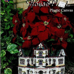 May include: A craft project featuring a miniature house made of plastic canvas, with a red poinsettia plant on top. The house is white with green and red accents. Text on the image reads "Holiday House Plot" and "Plastic Canvas".