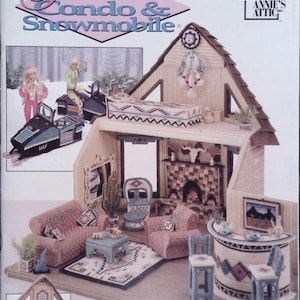 May include: A dollhouse with a condo and snowmobile theme. The dollhouse has a light brown exterior with a detailed interior, including a living room with pink furniture, a fireplace, and a bar area. The text "Fashion Doll Condo & Snowmobile" is at the top.