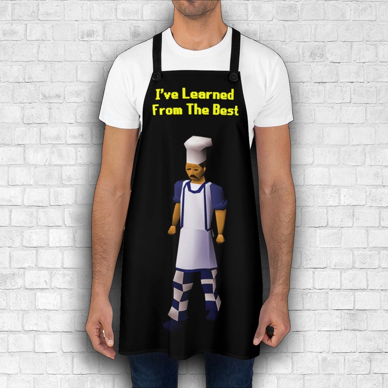 K&ouml;nnte beinhalten: Schwarze Sch&uuml;rze mit einer wei&szlig;en Kochfigur, die einen wei&szlig;en Hut und eine blau-wei&szlig; gestreifte Hose tr&auml;gt. Der Text "I've Learned From The Best" ist in Gelb auf der Sch&uuml;rze aufgedruckt.