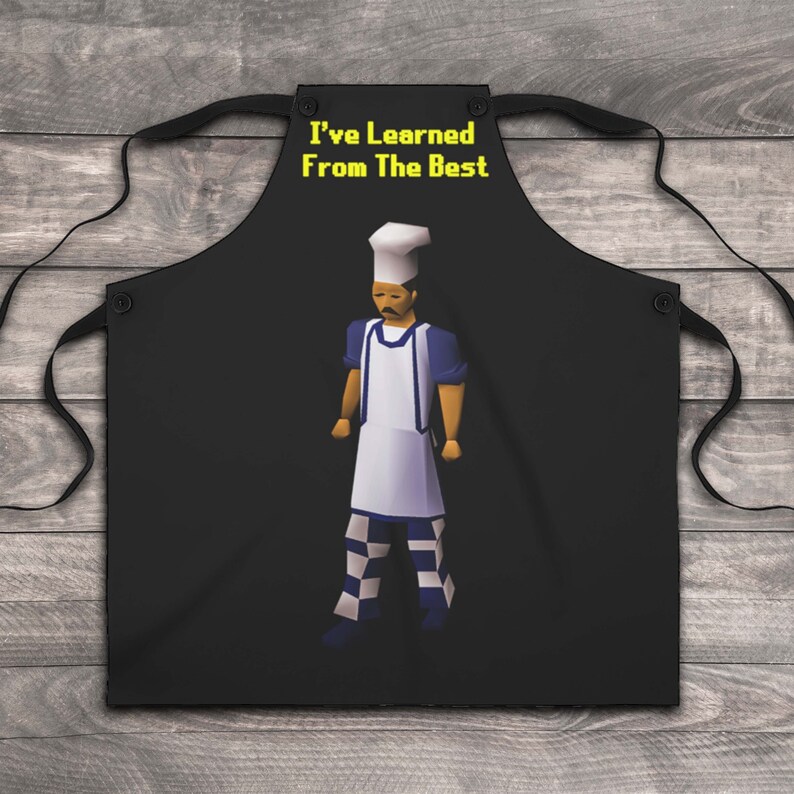 K&ouml;nnte beinhalten: Schwarze Sch&uuml;rze mit gelbem Text "I've Learned From The Best" und einer pixelartigen Kochfigur, die einen wei&szlig;en Kochhut, ein blaues Hemd, eine wei&szlig;e Sch&uuml;rze und eine karierte Hose tr&auml;gt.