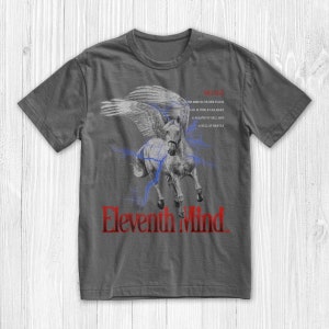 May include: A dark grey t-shirt featuring a red and white graphic of a winged horse with lightning bolts. The text "Eleventh Mind" is printed in red below the horse. The text "MIND" is printed in red at the top of the shirt, with a quote about the mind in smaller red text below it.