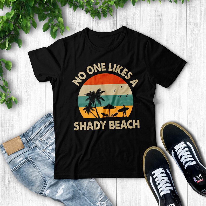 May include: Black t-shirt with a retro-style graphic of a palm tree and a surfer on a beach. The text "No one likes a shady beach" is printed on the shirt.