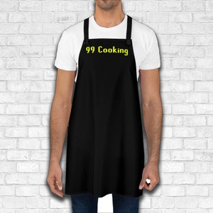 K&ouml;nnte beinhalten: Eine schwarze Sch&uuml;rze mit verstellbaren Tr&auml;gern und zwei Kn&ouml;pfen. Die Sch&uuml;rze tr&auml;gt den Text "99 Cooking" in Gelb.