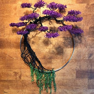 May include: A wire sculpture of a tree with purple leaves and green cascading branches. The tree is attached to a silver metal ring.