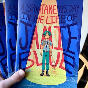 May include: A blue and orange comic book titled "A Spontaneous Day in the Life of Jamie Blue" with a cartoon character on the cover. The comic is by Noah Wilson.