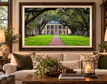 May include: A large rectangular framed wall art print featuring a white antebellum mansion at the end of a brick path, framed by a canopy of large oak trees with green grass, displayed in a dark wood frame with a wide white matting border.