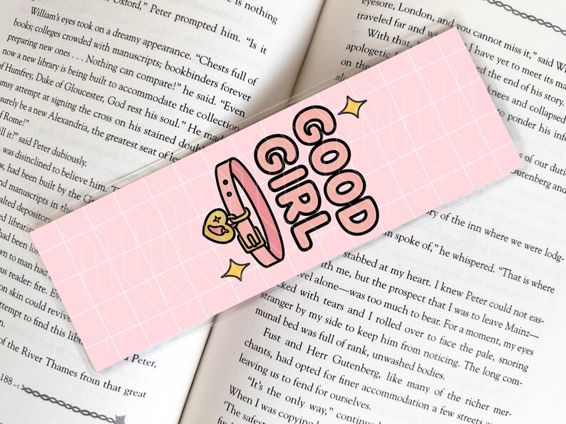 Pode incluir: Marcador de livros rosa com as palavras "GOOD GIRL" em letras pretas e rosa. O marcador apresenta uma coleira rosa com um pingente em forma de cora&ccedil;&atilde;o e detalhes dourados. Duas estrelas douradas tamb&eacute;m est&atilde;o inclu&iacute;das.