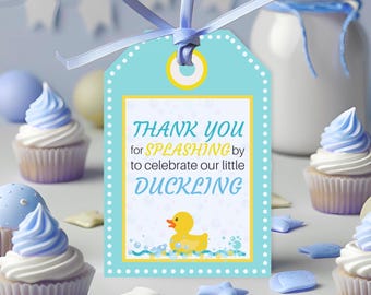 May include: A light blue gift tag with the text "THANK YOU for SPLASHING by to celebrate our little DUCKLING". The tag has a yellow border and a yellow rubber duck illustration. Cupcakes with blue frosting and star-shaped candies are in the background.