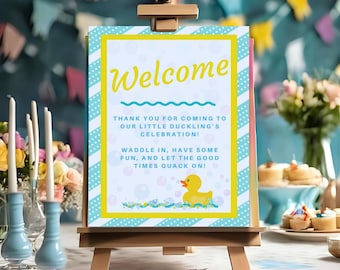 May include: A welcome sign on a wooden easel with the text "Welcome" in yellow script. The sign has a blue and white striped border and includes the phrases "Thank you for coming to our little duckling's celebration!" and "Waddle in, have some fun, and let the good times quack on!"