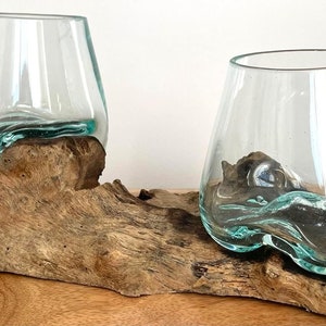 May include: Two clear glass vases with a wavy, irregular rim sit on a piece of driftwood. The driftwood is brown and has a natural, rough texture.