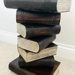 May include: A dark brown wooden side table in the shape of a stack of books. The books have textured, off-white pages and are arranged in a staggered pile. A unique decorative accent for a room.