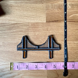 Puede incluir: Un peque&ntilde;o azulejo de cer&aacute;mica marr&oacute;n y negro que representa el Golden Gate Bridge. El azulejo mide aproximadamente 7,6 cm de largo y 2,5 cm de ancho.