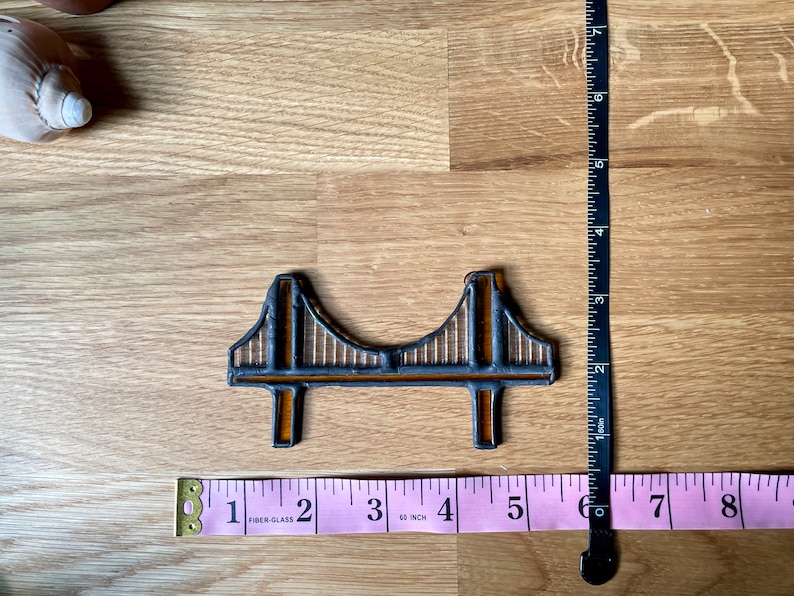 Puede incluir: Un peque&ntilde;o azulejo de cer&aacute;mica marr&oacute;n y negro que representa el Golden Gate Bridge. El azulejo mide aproximadamente 7,6 cm de largo y 2,5 cm de ancho.