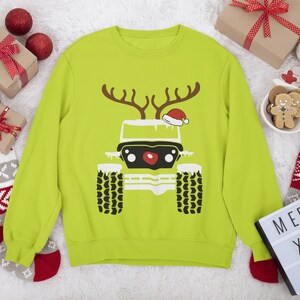 Puede incluir: Un su&eacute;ter navide&ntilde;o verde lima con una silueta negra y blanca de un jeep. El jeep tiene una nariz roja y un gorro de Pap&aacute; Noel rojo en la parte superior. El jeep tiene cuernos y est&aacute; cubierto de nieve.