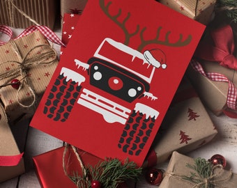 Puede incluir: Una tarjeta de Navidad roja con una ilustración en blanco y negro de un jeep con cuernos de reno y un gorro de Papá Noel. La tarjeta está rodeada de regalos envueltos con papel rojo y marrón y cinta roja.