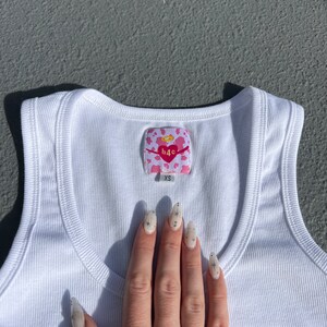 May include: White ribbed tank top with a pink and white heart-shaped tag that says "h4c" and "XS".