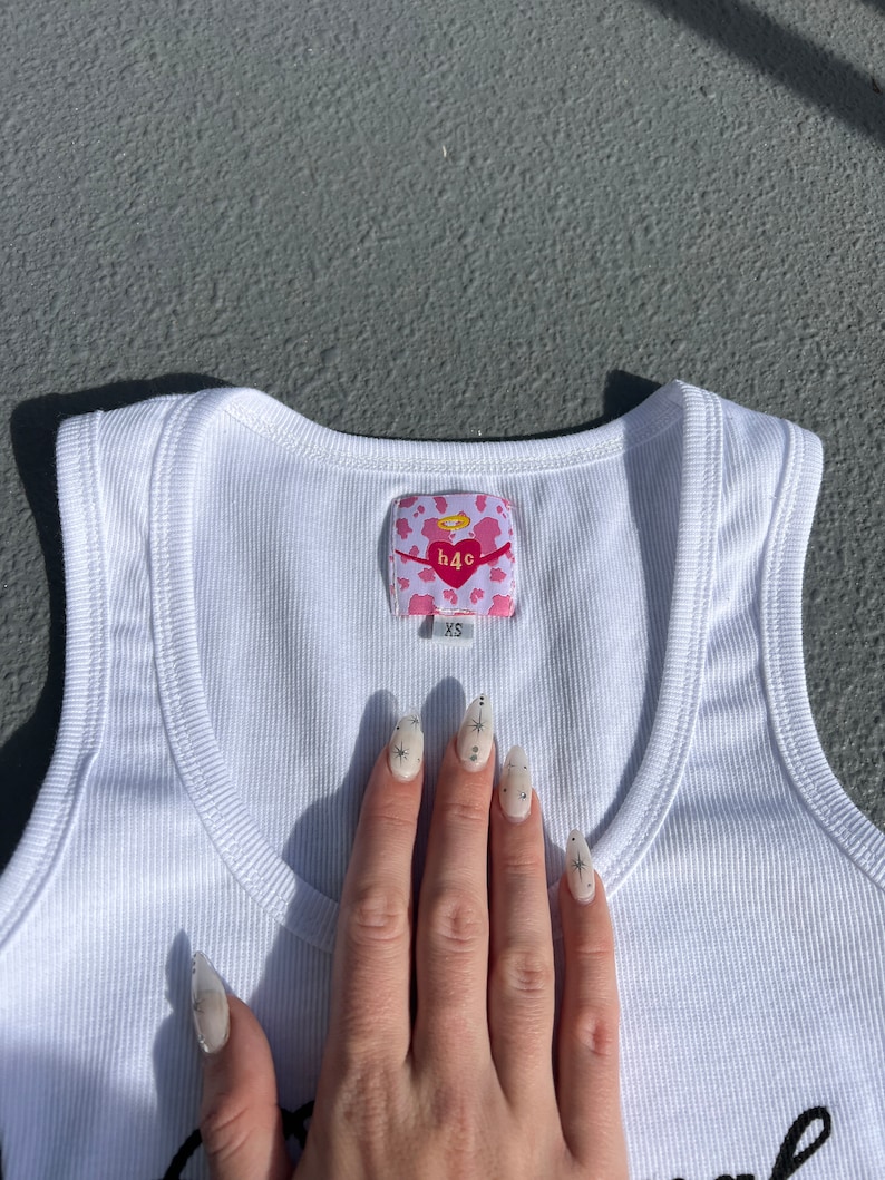 May include: White ribbed tank top with a pink and white heart-shaped tag that says "h4c" and "XS".