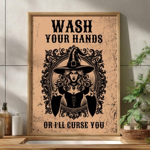 May include: A framed poster with the text "WASH YOUR HANDS OR I'LL CURSE YOU." The poster features a witch illustration in a decorative frame. The background is a light peach color, and the text and illustration are black.