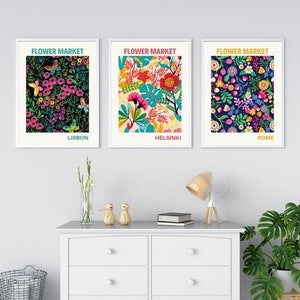 May include: Three framed floral prints with the title "Flower Market" and the city names "Lisbon", "Helsinki", and "Rome" underneath. The prints are hanging on a white wall above a white dresser with six drawers.