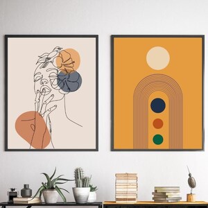 May include: Two framed abstract art prints. The print on the left features a line drawing of a woman's face with a bird and flowers. The print on the right features a rainbow arch with three circles in a yellow background.